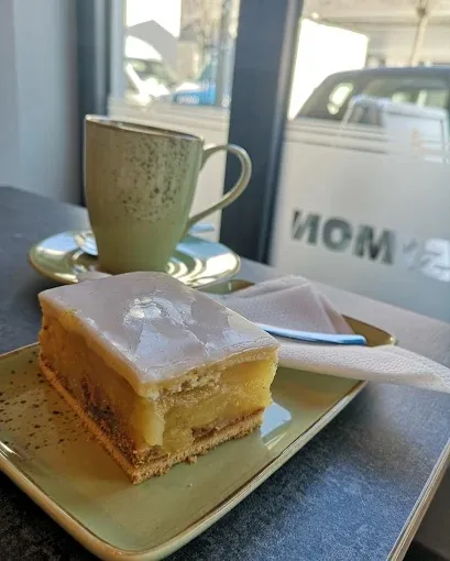 Ein Stück Apfelkuchen mit Zuckerguss und eine Tasse Kaffee am Fenster